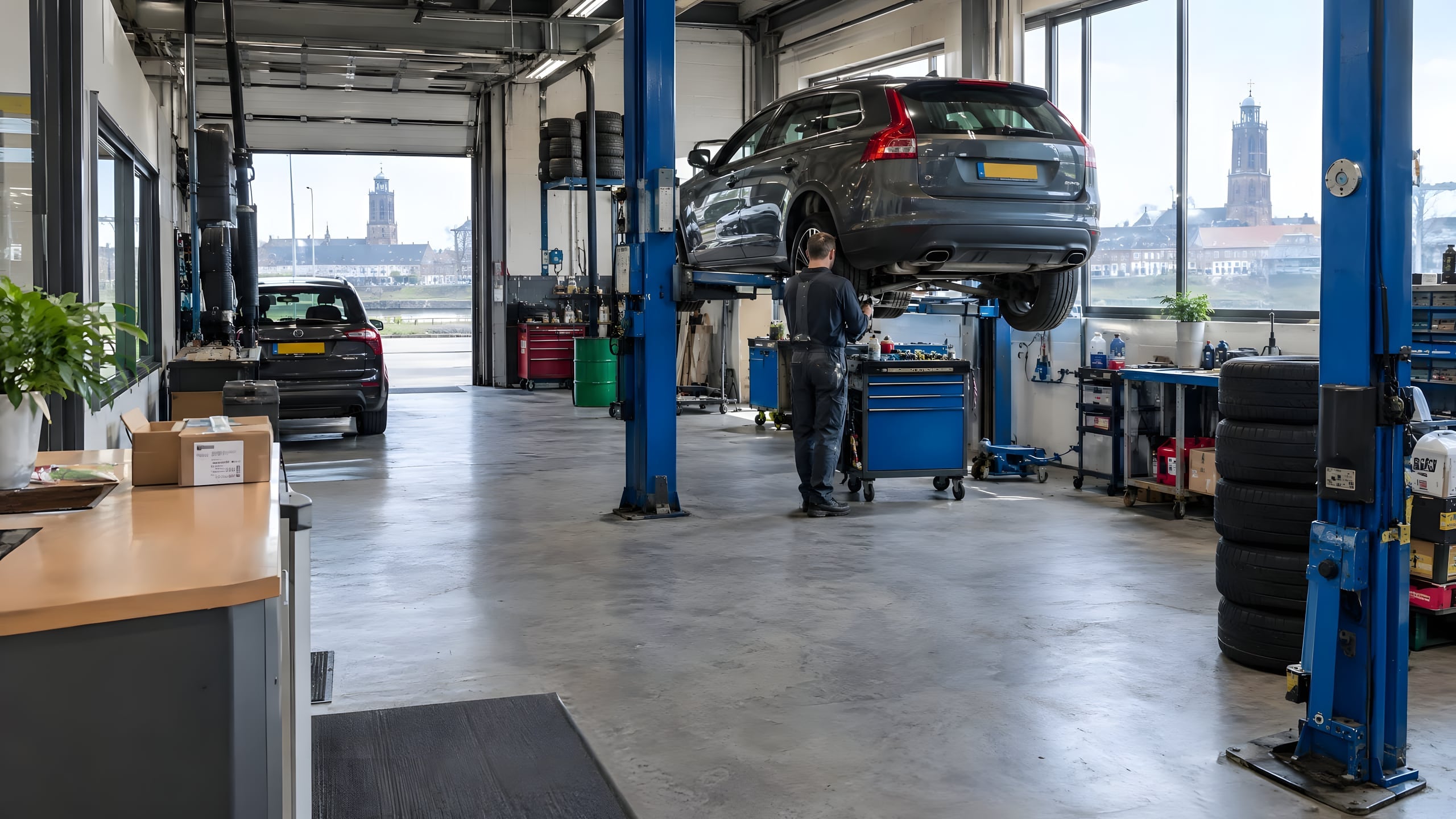 Werkplaats met een auto op de hefbrug en een monteur aan het werk
